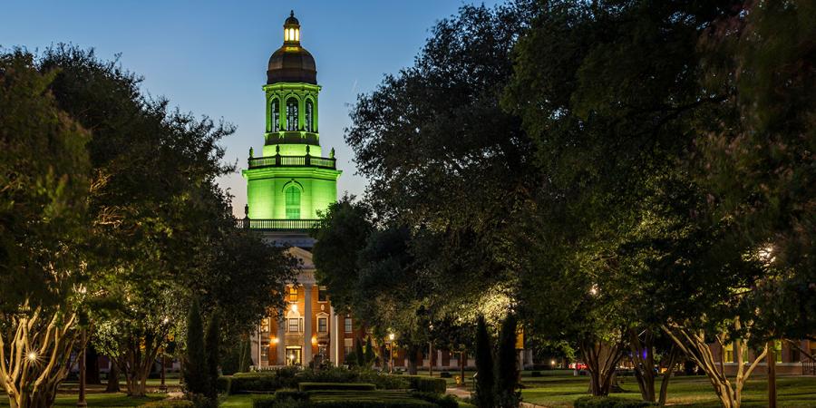Pat Neff Hall lit green at dusk, with the Sadie Jo Black Gardens in the foreground