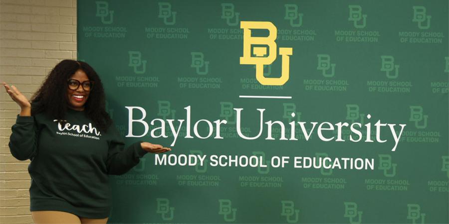 A professor stands next to a sign reading Baylor University Moody School of Education