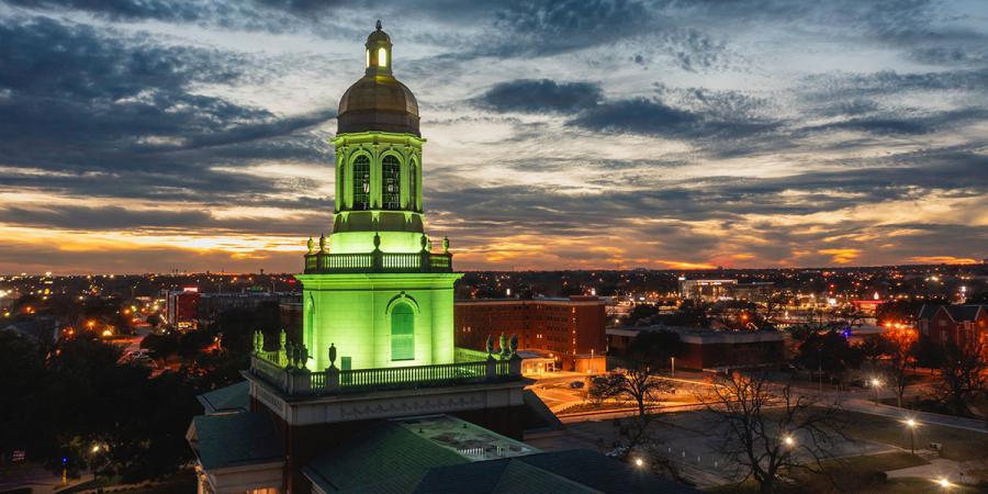 Drone photo of Pat Neff Hall lit green at sunset