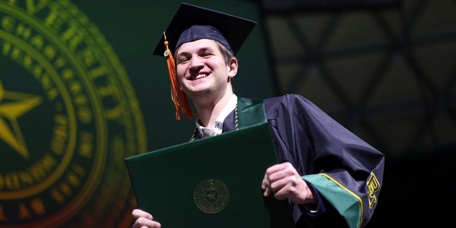 A Baylor graduate smiles as he crosses the stage with his diploma